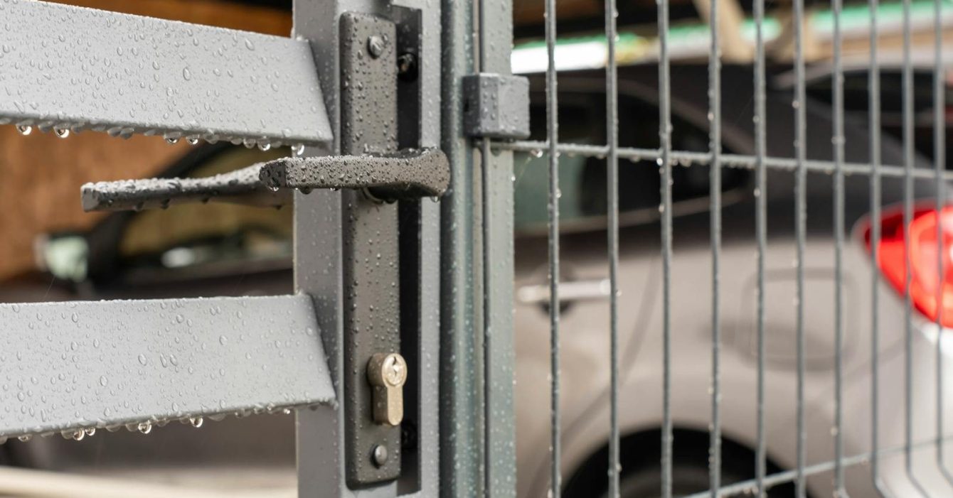 Photo by Vladimir Srajber Detailed view of a wet metal gate with raindrops and a parked car in the background.