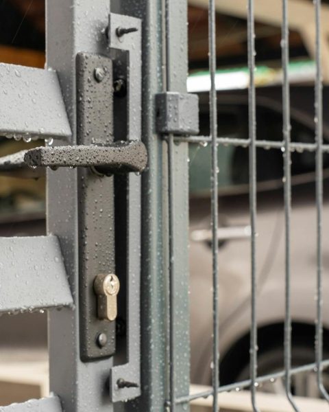 Detailed view of a wet metal gate with raindrops and a parked car in the background.