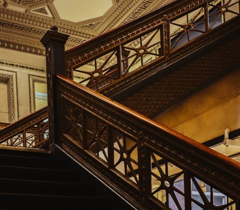 Photo by Daniel Romero Wooden staircase ascends towards a patterned ceiling.