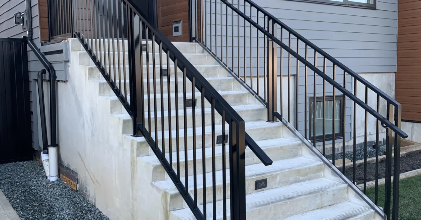 Modern concrete outdoor staircase with a minimalist satin black aluminum railing.