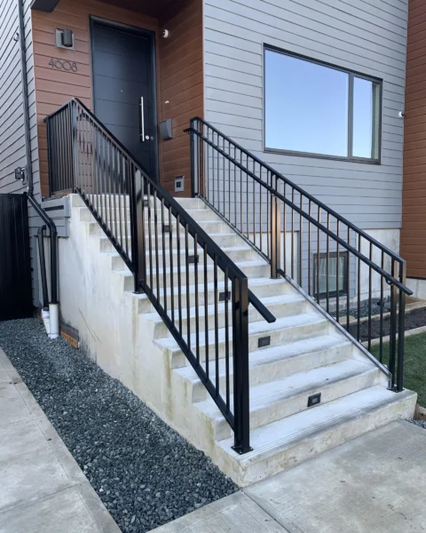 Modern concrete outdoor staircase with a minimalist satin black aluminum railing.